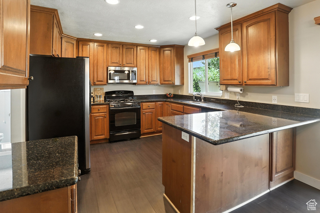 Kitchen featuring stainless steel appliances, a peninsula, recessed lighting, brown cabinetry, and dark wood finished floors