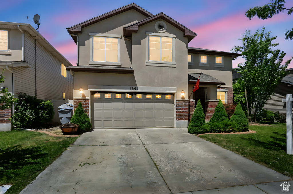 Traditional-style house featuring brick siding, stucco siding, an attached garage, concrete driveway, and a yard
