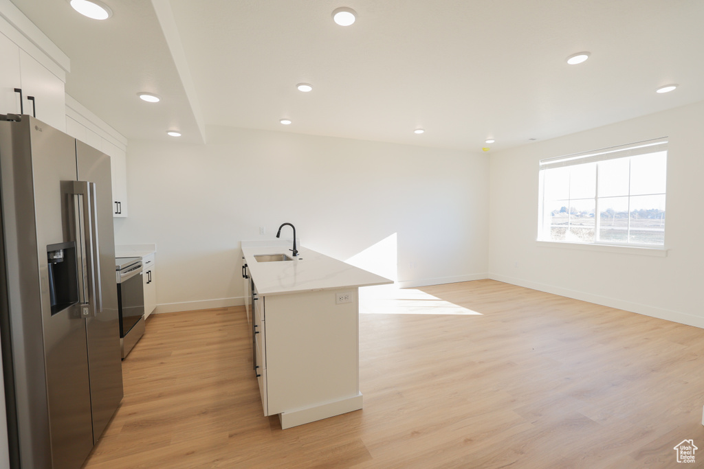 Kitchen with appliances with stainless steel finishes, white cabinetry, light countertops, light wood finished floors, and recessed lighting
