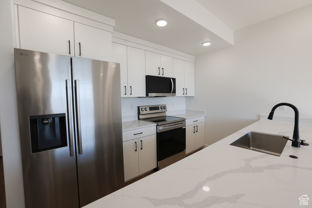 Kitchen with appliances with stainless steel finishes, white cabinets, light stone countertops, and recessed lighting