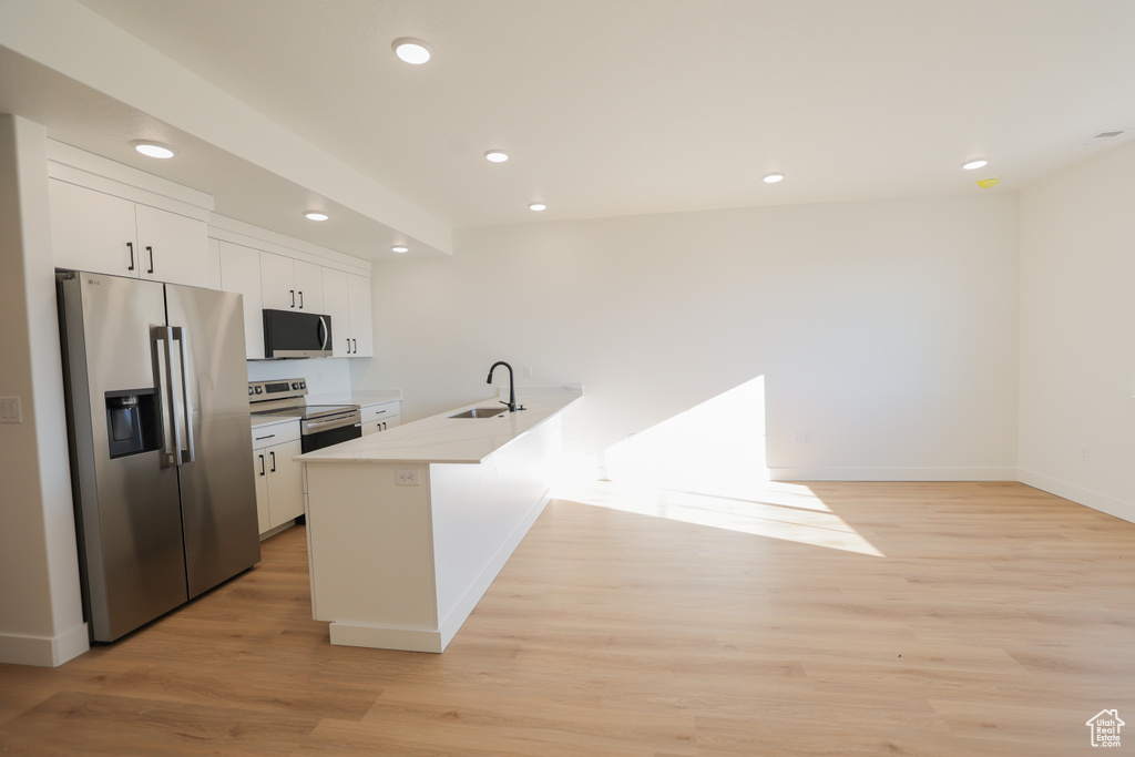 Kitchen with stainless steel appliances, a peninsula, white cabinets, recessed lighting, and light wood-type flooring