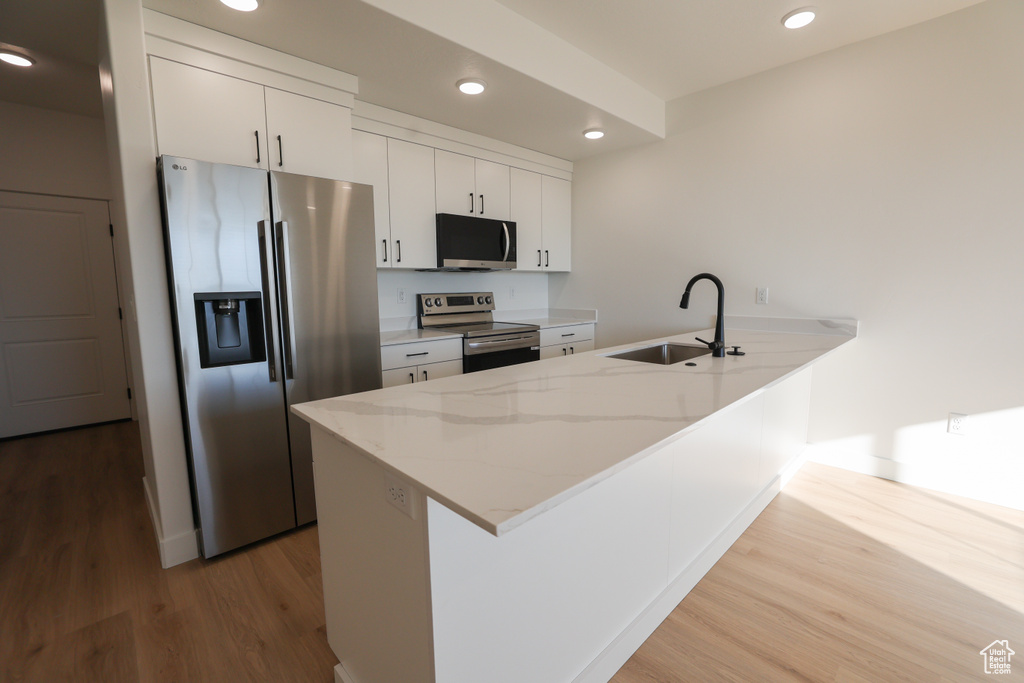 Kitchen featuring stainless steel appliances, a peninsula, wood finished floors, recessed lighting, and white cabinetry