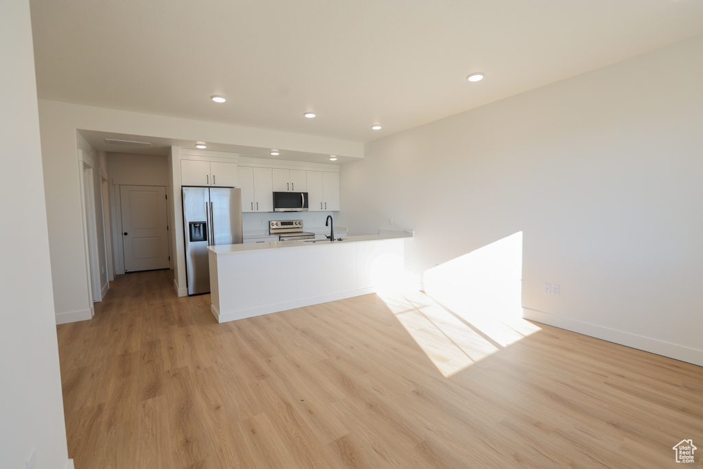 Kitchen featuring appliances with stainless steel finishes, recessed lighting, white cabinets, light wood-type flooring, and light countertops