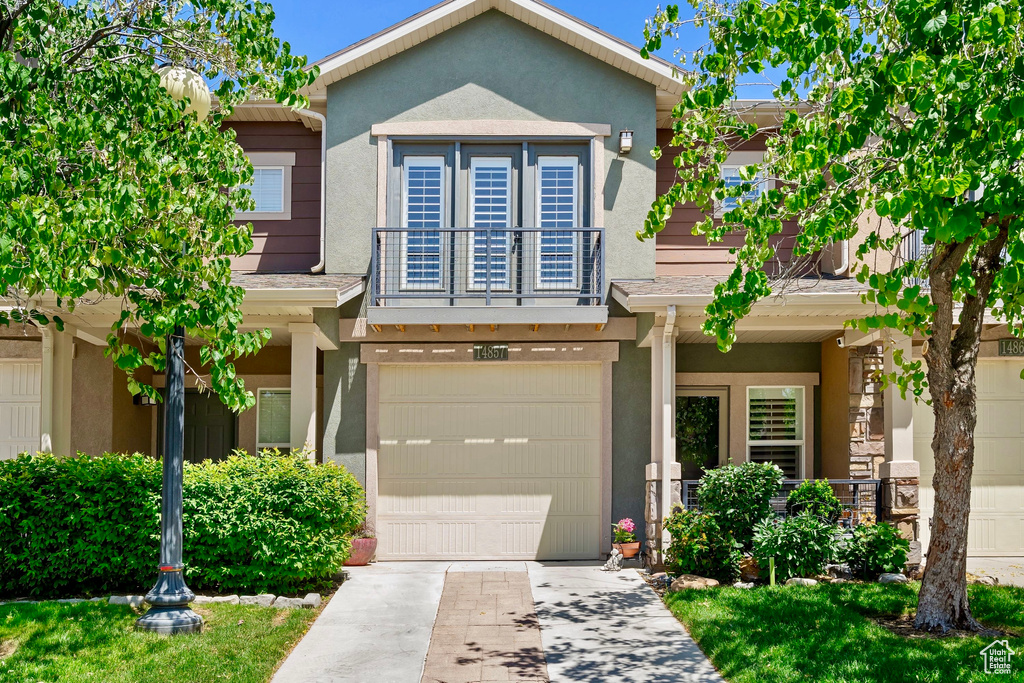 View of front of home featuring driveway, a balcony, stucco siding, and a garage
