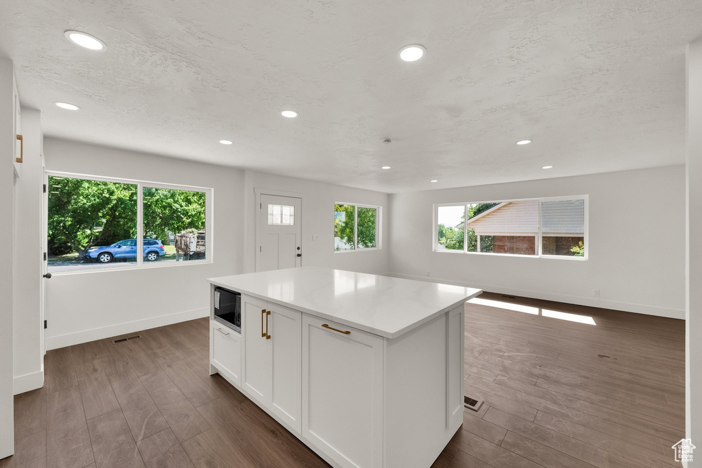 Kitchen featuring recessed lighting, white cabinetry, a center island, dark wood-type flooring, and light countertops