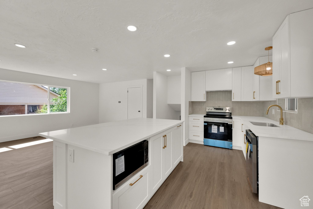 Kitchen with appliances with stainless steel finishes, wood finished floors, light countertops, white cabinetry, and recessed lighting
