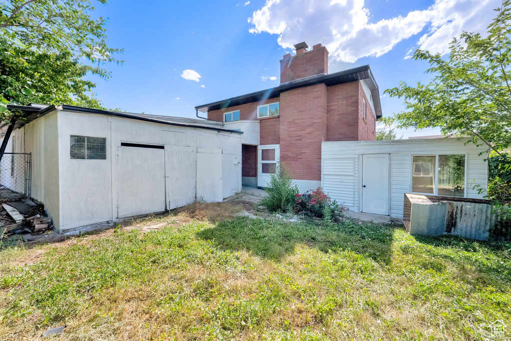 Rear view of property featuring a storage unit, a chimney, a yard, and brick siding