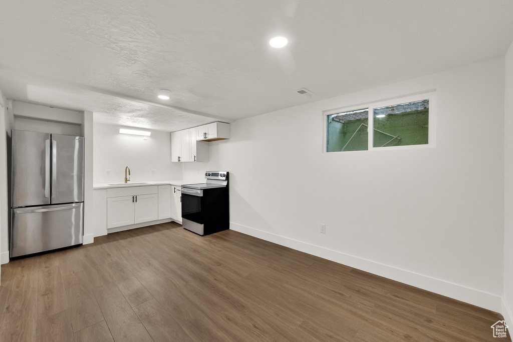 Kitchen featuring appliances with stainless steel finishes, wood finished floors, light countertops, white cabinetry, and recessed lighting