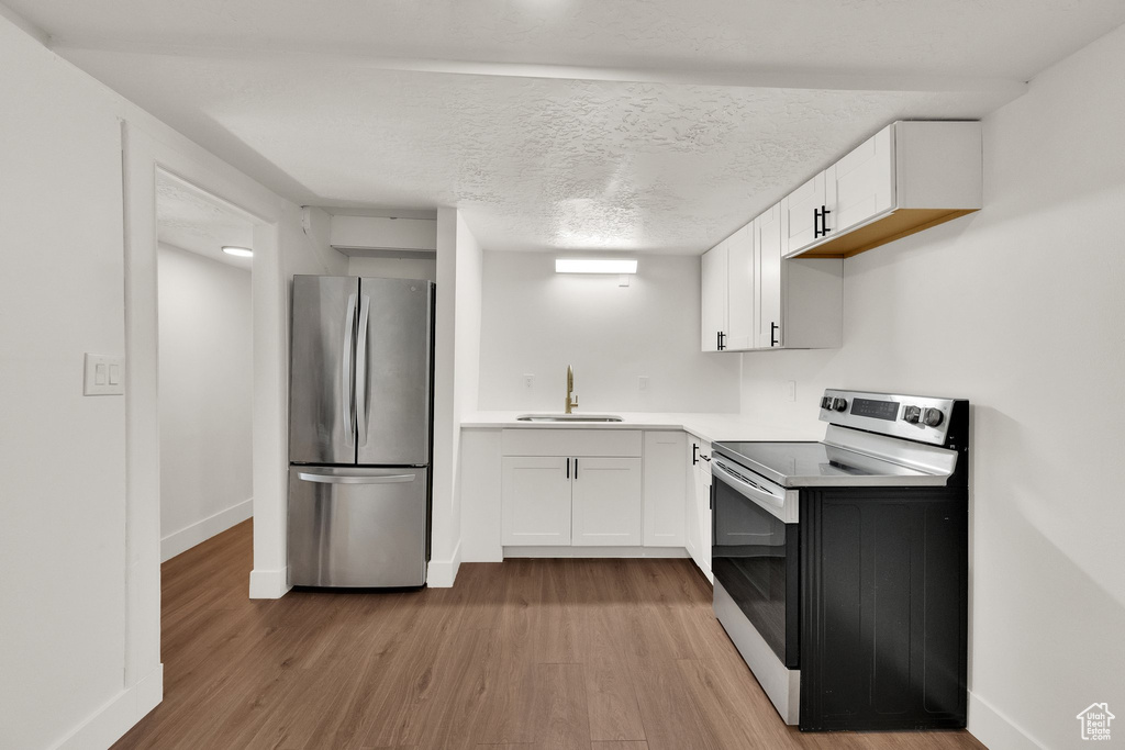 Kitchen featuring range with electric cooktop, freestanding refrigerator, light wood-style floors, white cabinets, and a textured ceiling