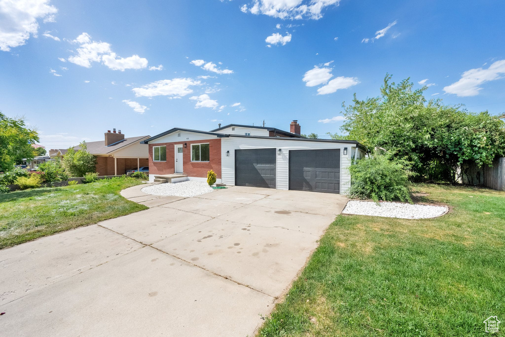 View of front facade with a front lawn, a garage, driveway, and a chimney