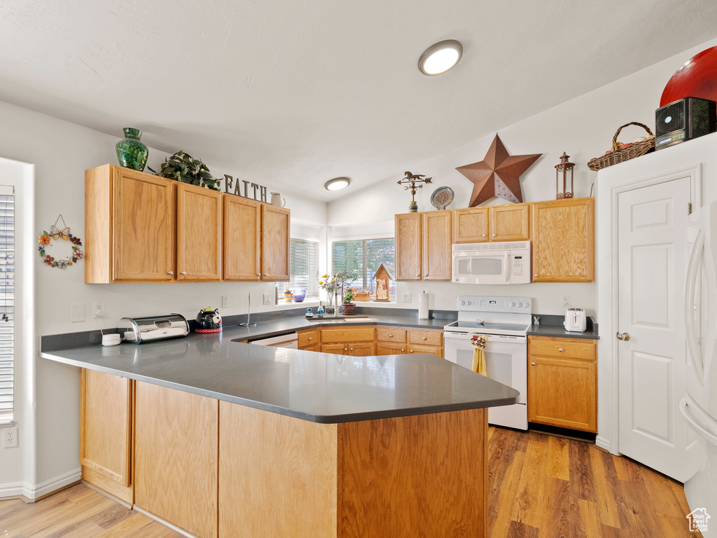 Kitchen featuring white appliances, a peninsula, light wood-style floors, and dark countertops