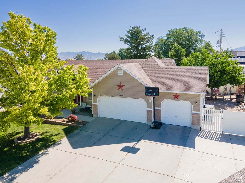 View of front facade featuring a gate, concrete driveway, roof with shingles, an attached garage, and brick siding