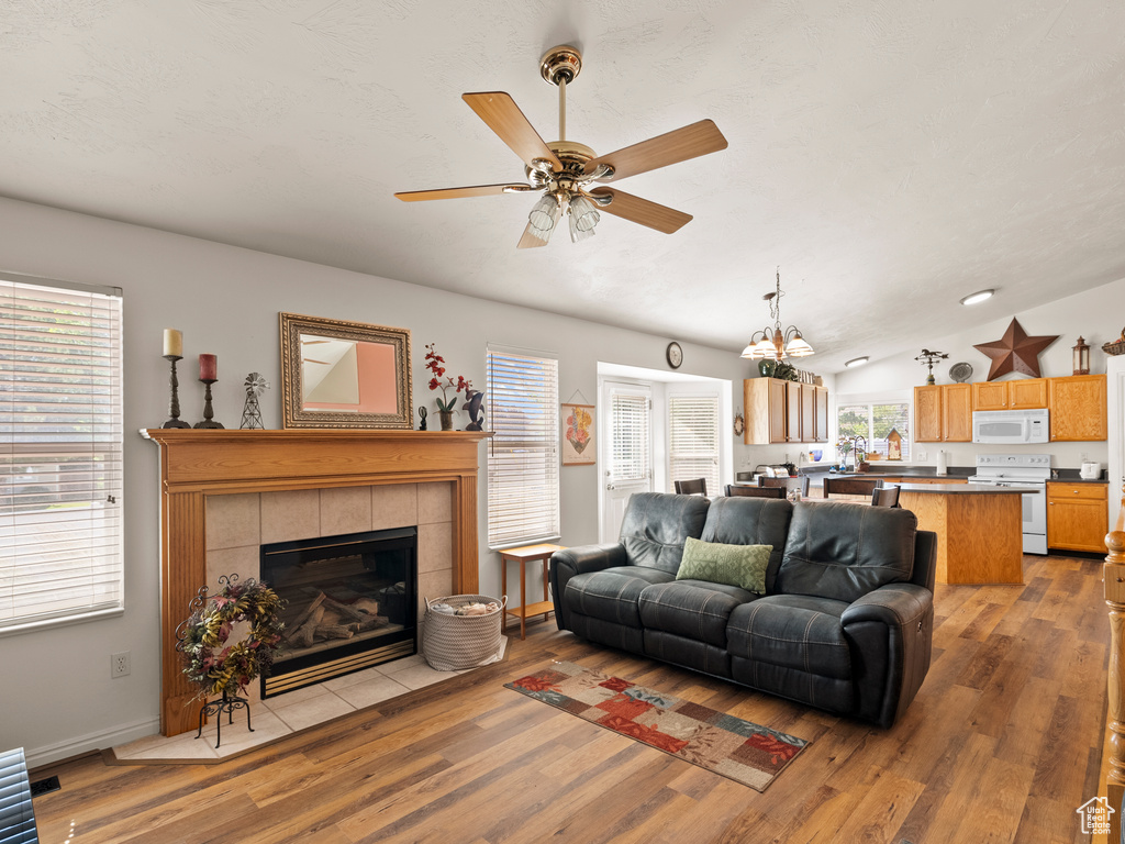 Living room with ceiling fan, light wood finished floors, a tiled fireplace, lofted ceiling, and a chandelier