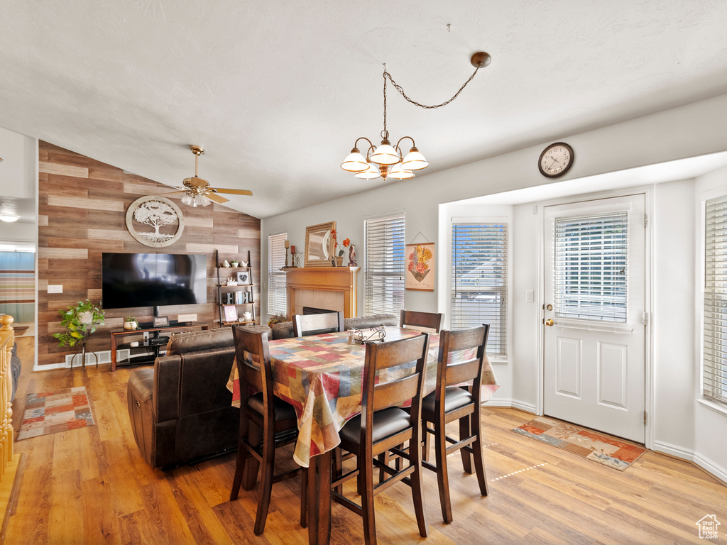 Dining area with light wood-style floors, wood walls, vaulted ceiling, a ceiling fan, and a chandelier