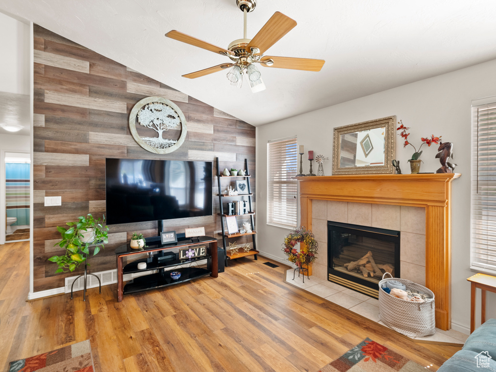 Living room featuring wooden walls, wood finished floors, a ceiling fan, a fireplace, and high vaulted ceiling