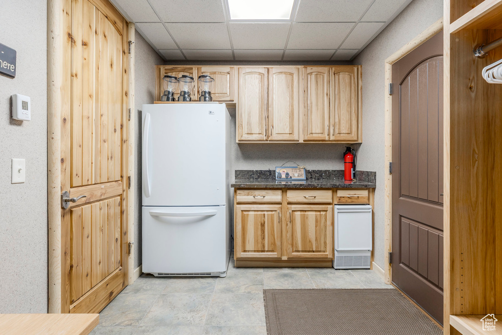 Kitchen with freestanding refrigerator, a drop ceiling, and dark stone countertops