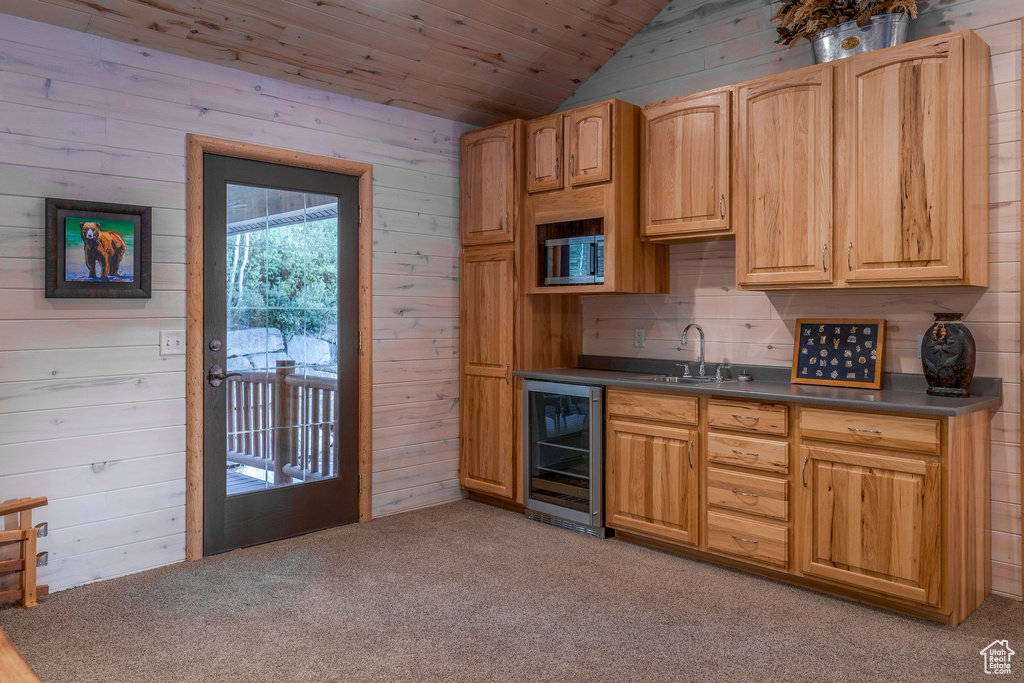 Kitchen featuring wine cooler, lofted ceiling, wooden walls, light carpet, and dark countertops