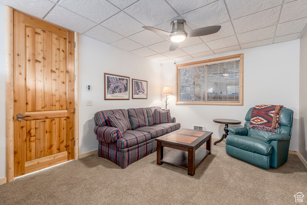 Carpeted living area featuring ceiling fan and a paneled ceiling