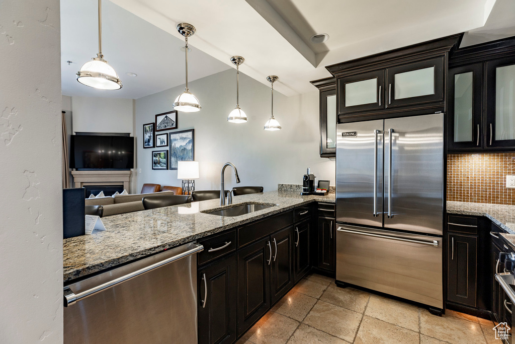 Kitchen featuring appliances with stainless steel finishes, decorative backsplash, light stone countertops, glass insert cabinets, and hanging light fixtures