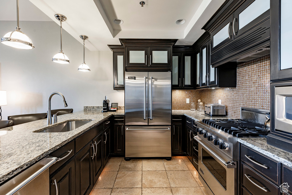 Kitchen with high end appliances, glass insert cabinets, hanging light fixtures, and tasteful backsplash