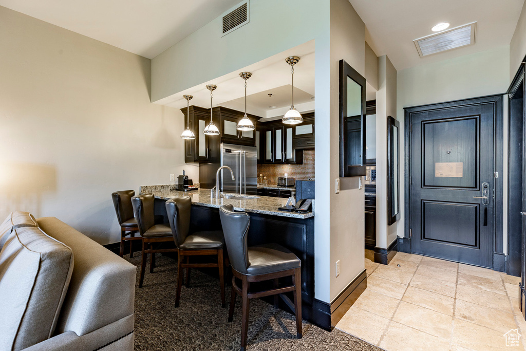 Kitchen featuring stainless steel built in fridge, a breakfast bar area, tasteful backsplash, a peninsula, and light stone countertops
