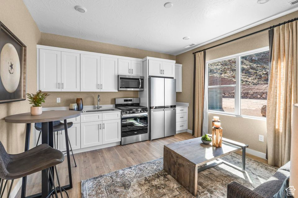 Kitchen with stainless steel appliances, light wood finished floors, and white cabinets