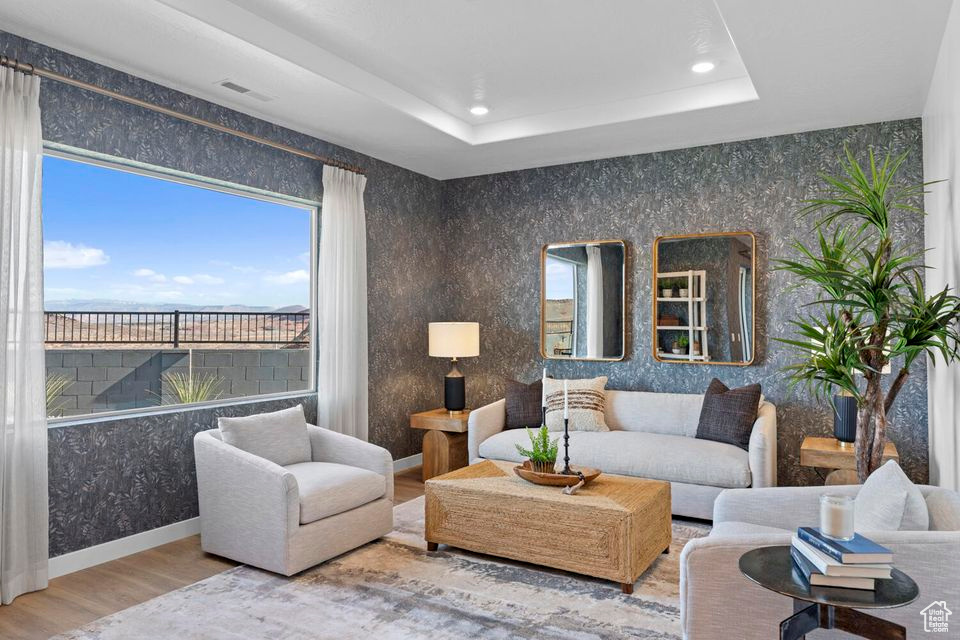 Living room with wood finished floors, recessed lighting, a raised ceiling, and wallpapered walls