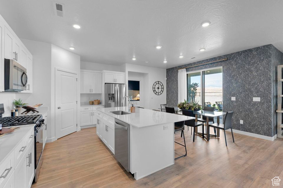 Kitchen with appliances with stainless steel finishes, an island with sink, light wood finished floors, recessed lighting, and white cabinetry