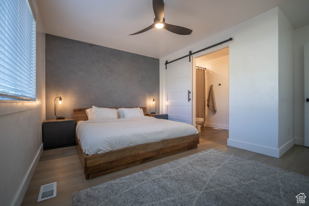 Bedroom featuring a barn door, wood finished floors, connected bathroom, and ceiling fan