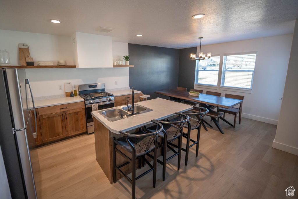 Kitchen with open shelves, appliances with stainless steel finishes, brown cabinetry, light wood-style floors, and a kitchen bar