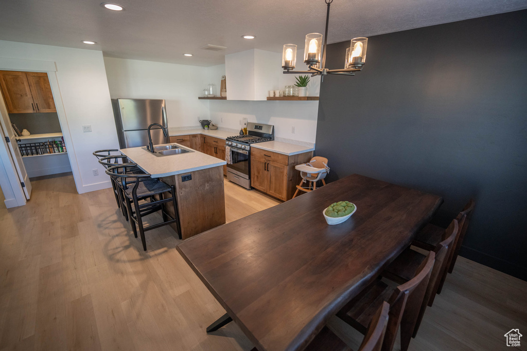 Kitchen with appliances with stainless steel finishes, open shelves, an island with sink, light wood-style flooring, and recessed lighting
