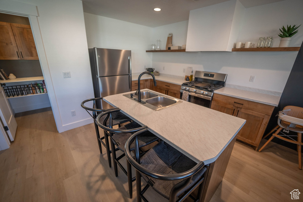 Kitchen with appliances with stainless steel finishes, open shelves, brown cabinetry, light wood-style flooring, and recessed lighting