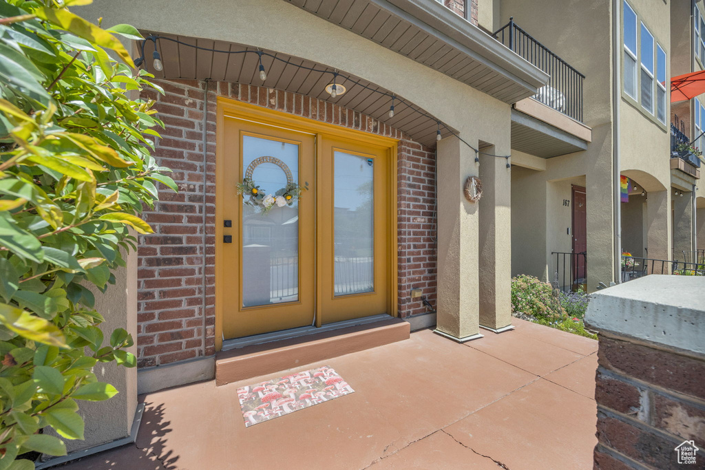 Doorway to property featuring stucco siding, brick siding, and a balcony