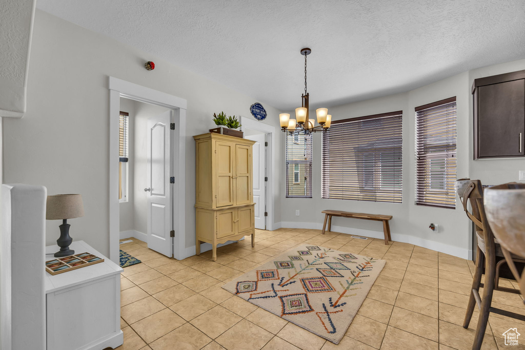 Dining area with light tile patterned flooring, a textured ceiling, a chandelier, and plenty of natural light