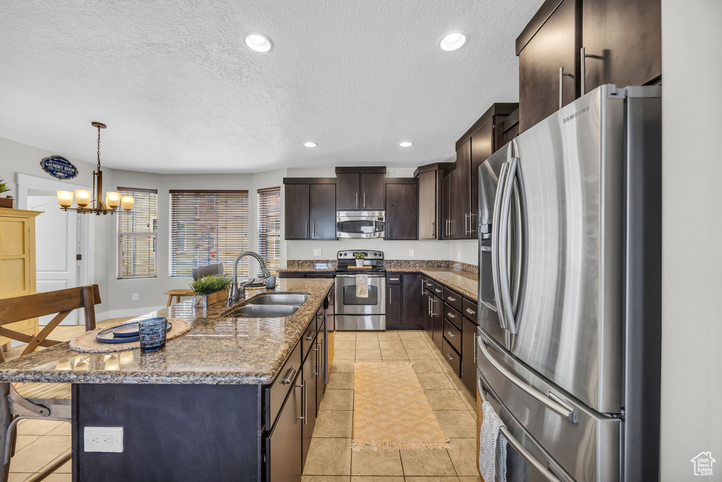 Kitchen with appliances with stainless steel finishes, a textured ceiling, dark stone countertops, dark brown cabinetry, and pendant lighting