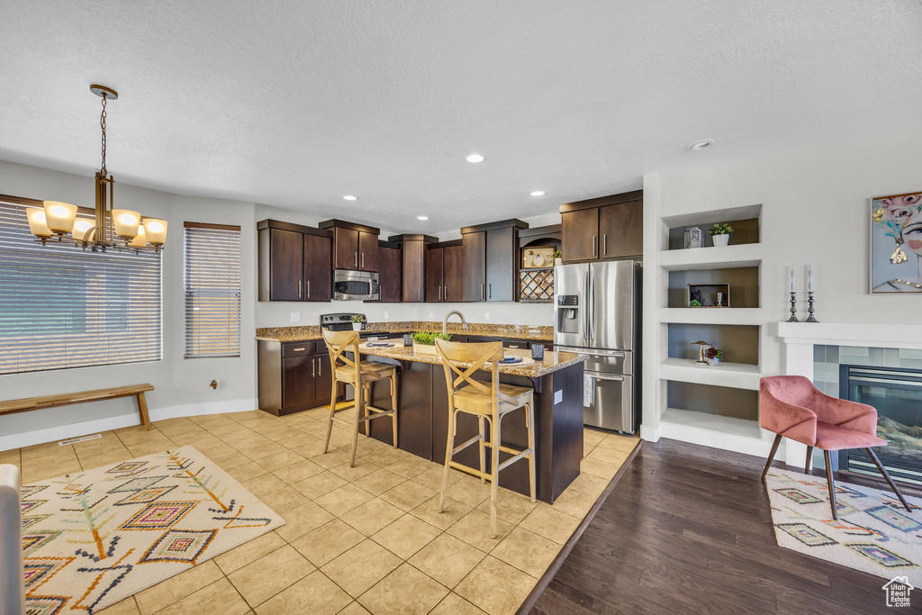 Kitchen featuring appliances with stainless steel finishes, open shelves, dark brown cabinets, a breakfast bar, and recessed lighting