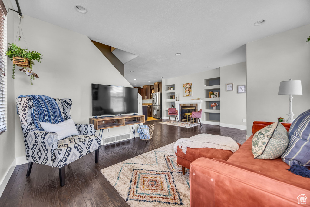 Living room with wood finished floors, a fireplace, built in shelves, and recessed lighting