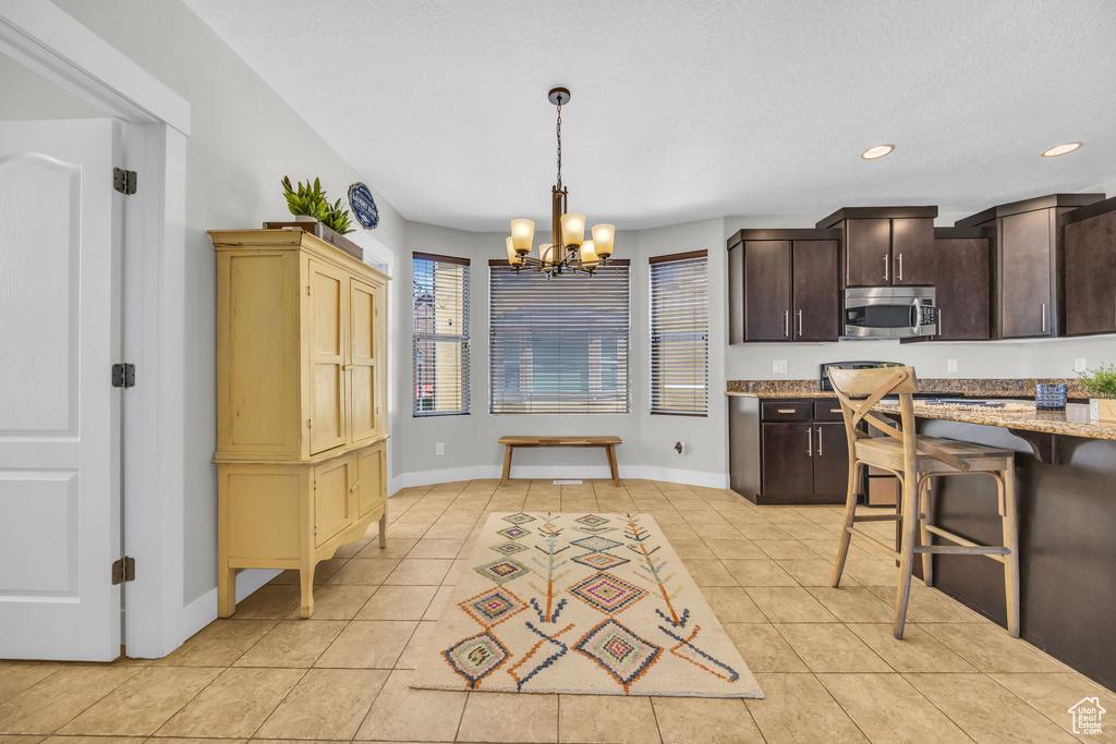 Kitchen with stainless steel microwave, a chandelier, light tile patterned floors, dark brown cabinets, and recessed lighting