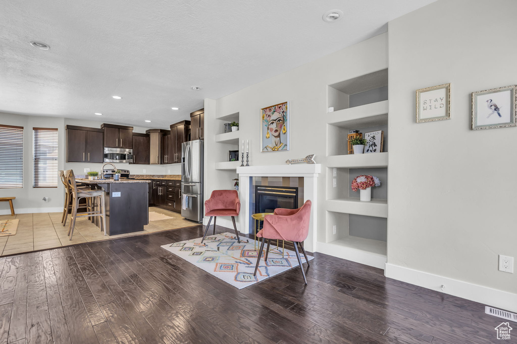 Living room with built in features, light wood-style floors, a glass covered fireplace, recessed lighting, and a textured ceiling