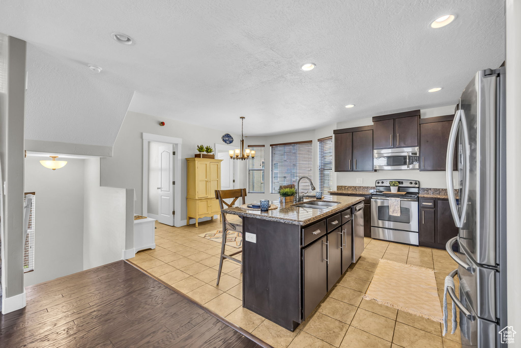 Kitchen with stainless steel appliances, a kitchen bar, dark brown cabinets, a chandelier, and stone counters