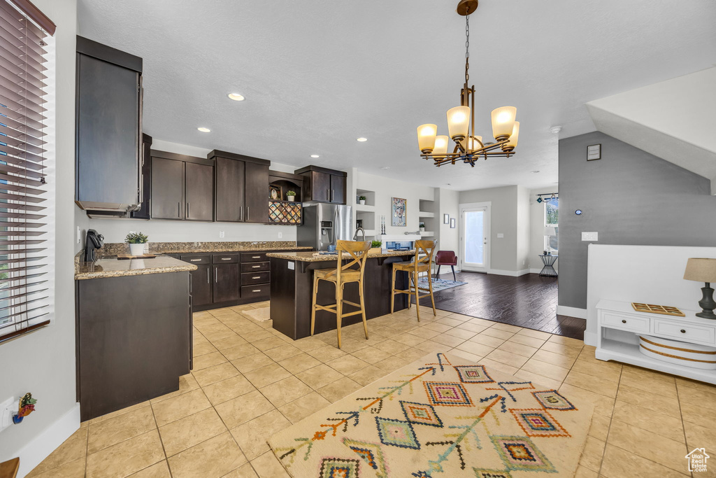 Kitchen with stainless steel fridge, light tile patterned floors, a kitchen bar, dark brown cabinetry, and recessed lighting