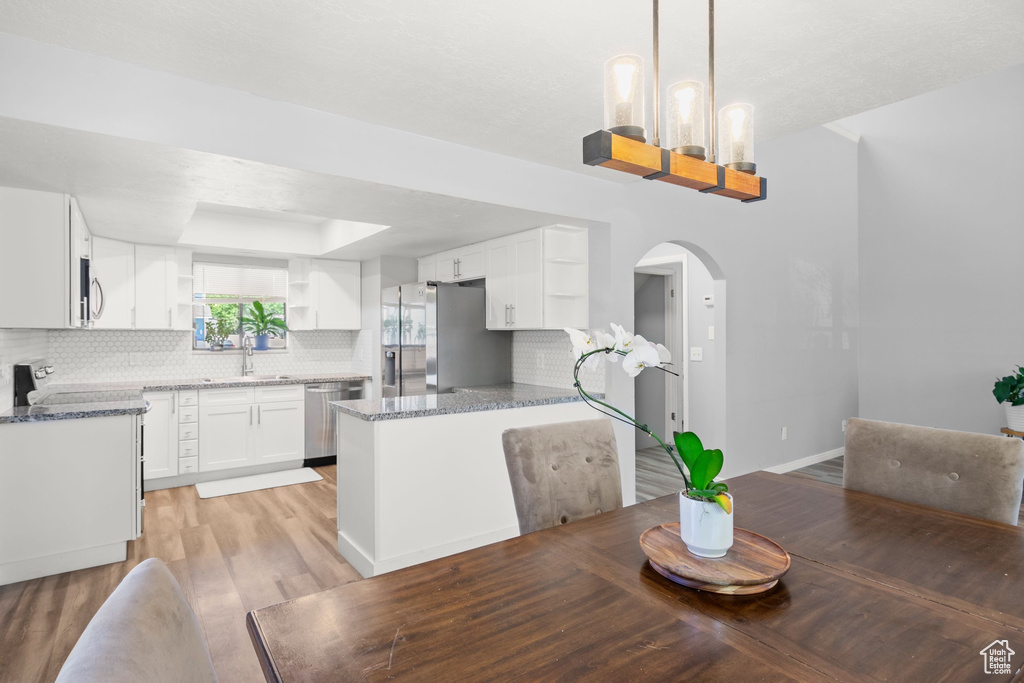 Dining area featuring arched walkways, light wood-style floors, a chandelier, and a tray ceiling