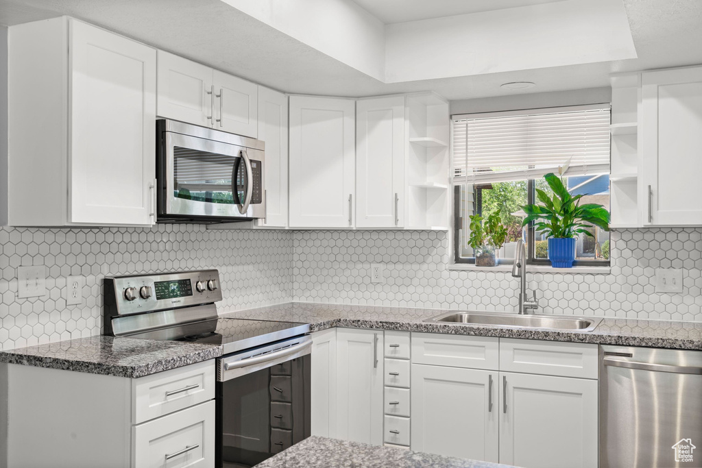 Kitchen featuring appliances with stainless steel finishes, open shelves, white cabinets, tasteful backsplash, and light stone counters
