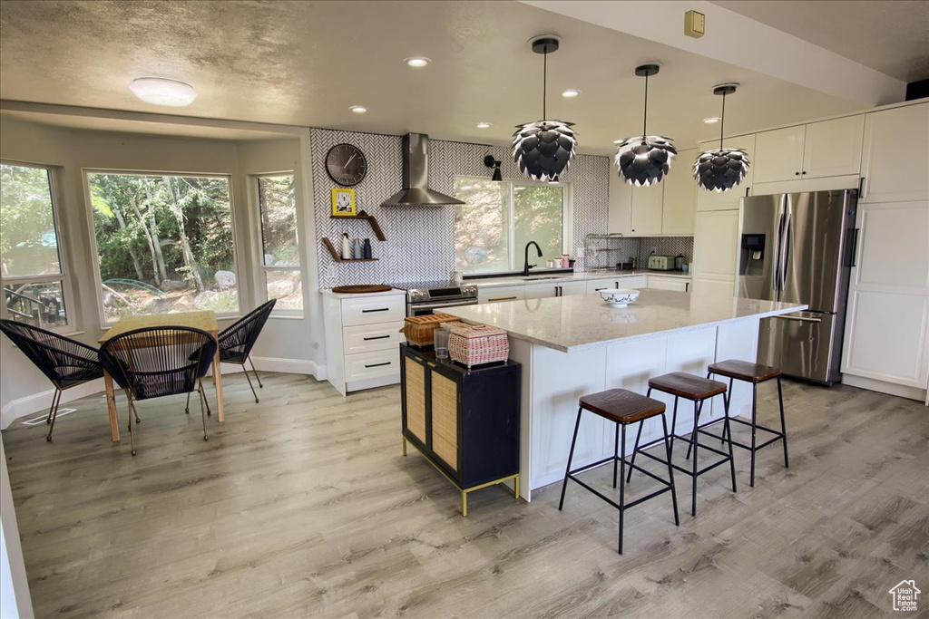 Kitchen with stainless steel appliances, wall chimney exhaust hood, plenty of natural light, white cabinetry, and recessed lighting