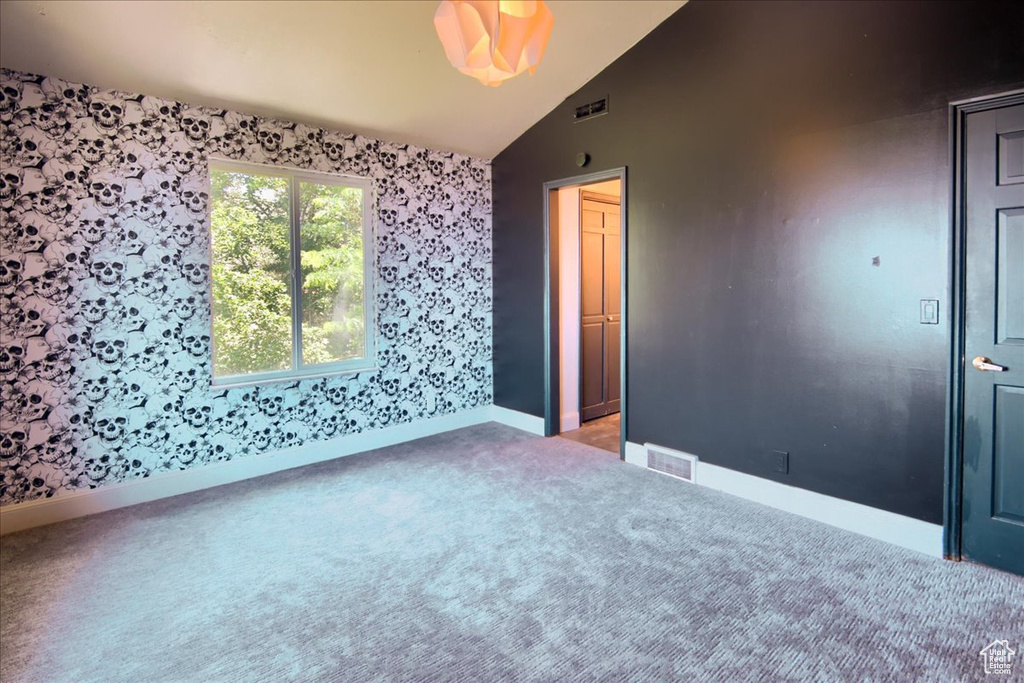 Spare room featuring light carpet, wallpapered walls, and lofted ceiling