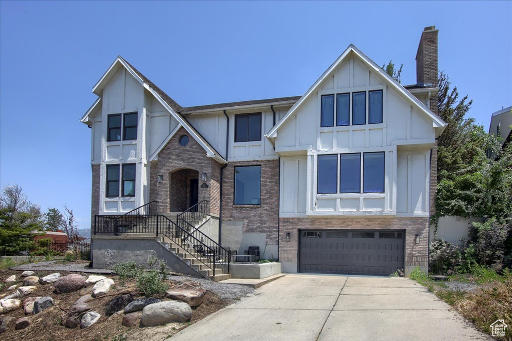 English style home featuring board and batten siding, an attached garage, concrete driveway, and brick siding
