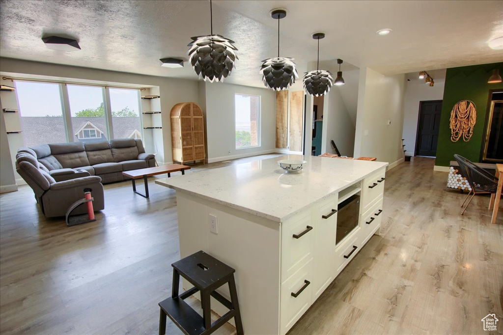 Kitchen featuring open floor plan, white cabinets, light wood-style floors, a center island, and recessed lighting