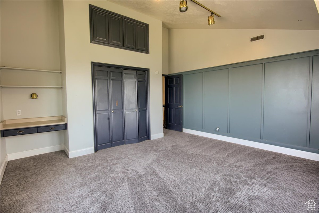 Unfurnished bedroom with carpet flooring, high vaulted ceiling, track lighting, and a closet