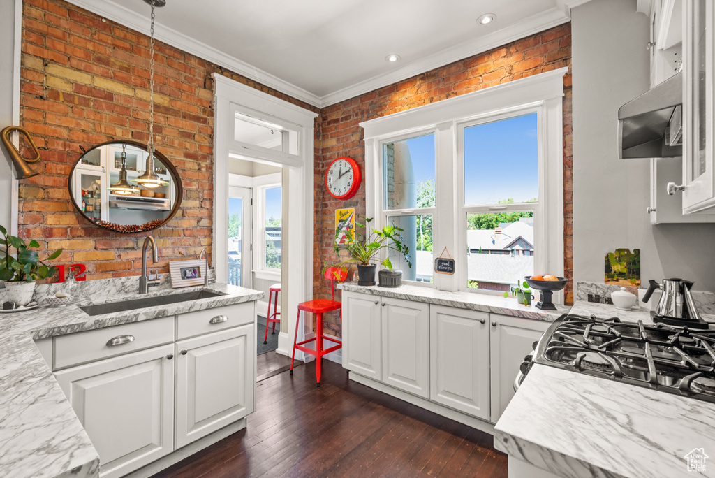 Kitchen featuring brick wall, white cabinets, extractor fan, ornamental molding, and dark wood-type flooring