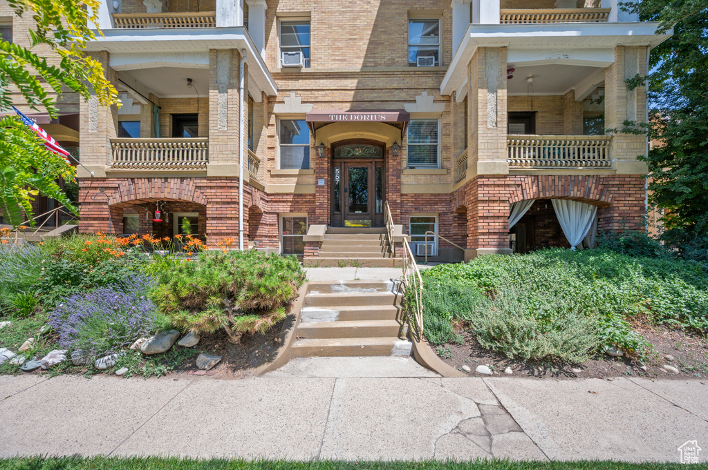 View of exterior entry with brick siding, a balcony, and cooling unit
